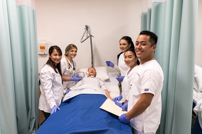 Students standing around a training dummy in a hospital bed