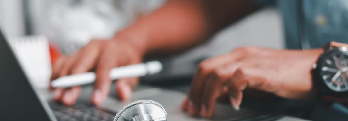 Close up of a male nurse with a stethoscope using a laptop