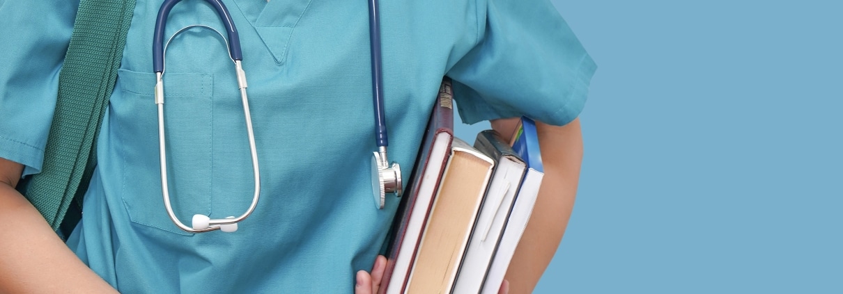 Nursing student in blue scrubs with a stack of books