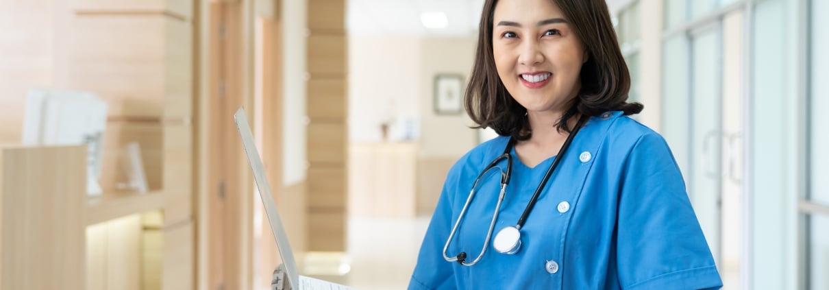 Asian nurse smiling with paperwork in a hospital hallway